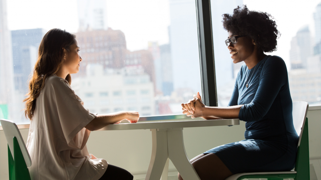 duas mulheres conversando em uma mesa fazendo gerência